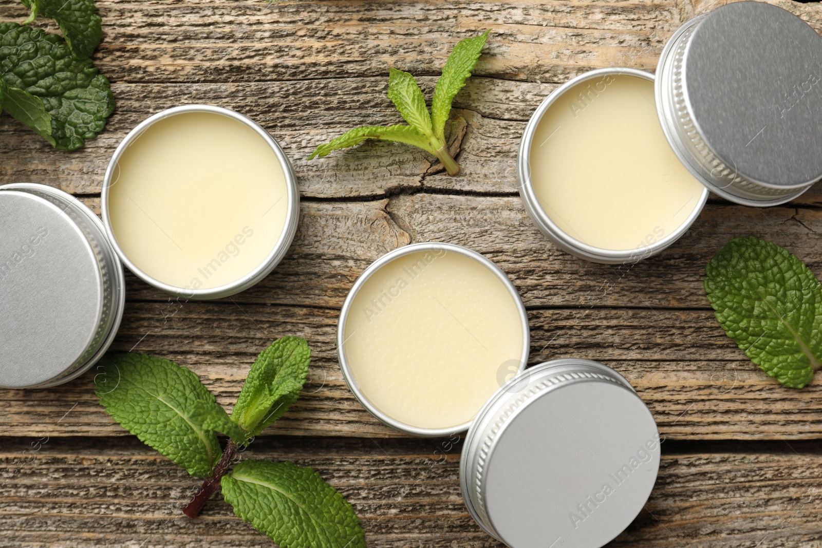 Photo of Natural lip balms and mint leaves on wooden background, flat lay