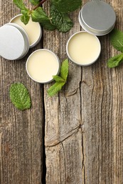 Photo of Natural lip balms and mint leaves on wooden background, flat lay. Space for text