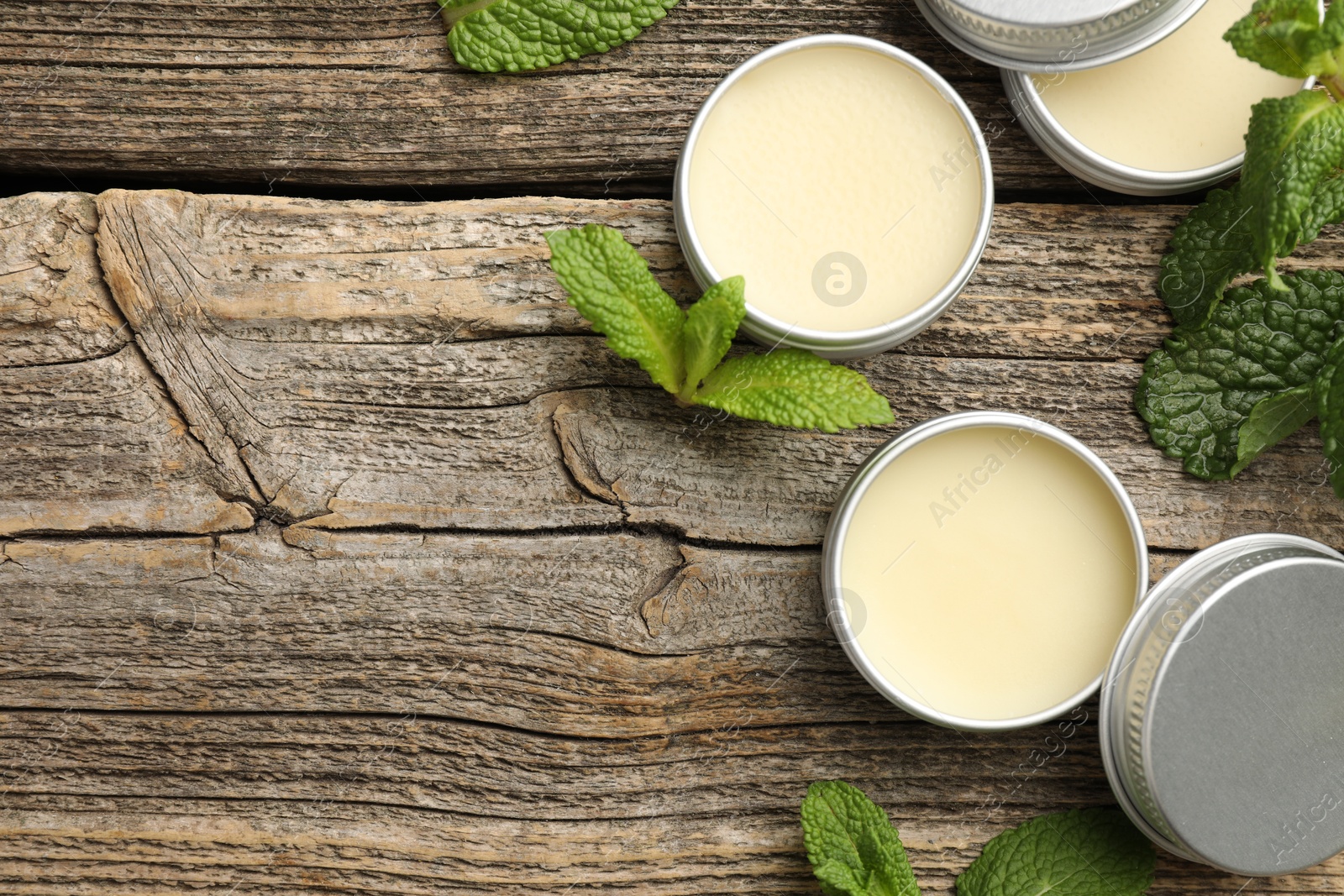 Photo of Natural lip balms and mint leaves on wooden background, flat lay. Space for text