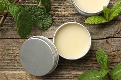 Natural lip balms and mint leaves on wooden background, flat lay