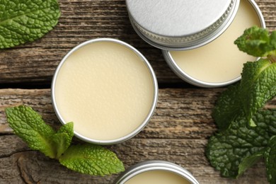 Photo of Natural lip balms and mint leaves on wooden background, flat lay