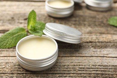 Photo of Natural lip balms and mint leaves on wooden background, selective focus