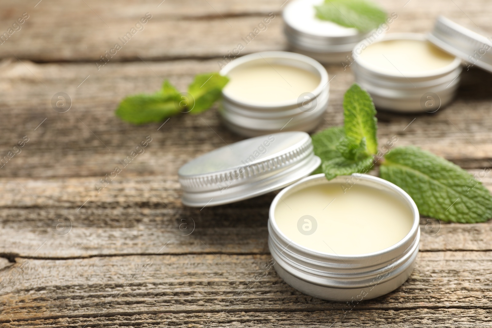 Photo of Natural lip balms and mint leaves on wooden background, selective focus. Space for text