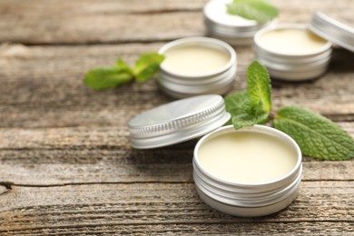 Photo of Natural lip balms and mint leaves on wooden background, selective focus. Space for text