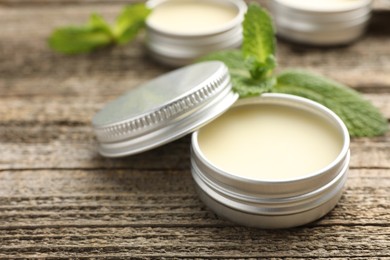 Photo of Natural lip balms and mint leaves on wooden background, selective focus