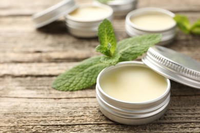 Photo of Natural lip balms and mint leaves on wooden background, selective focus. Space for text