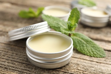 Photo of Natural lip balms and mint leaves on wooden background, selective focus