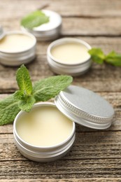 Photo of Natural lip balms and mint leaves on wooden background, selective focus