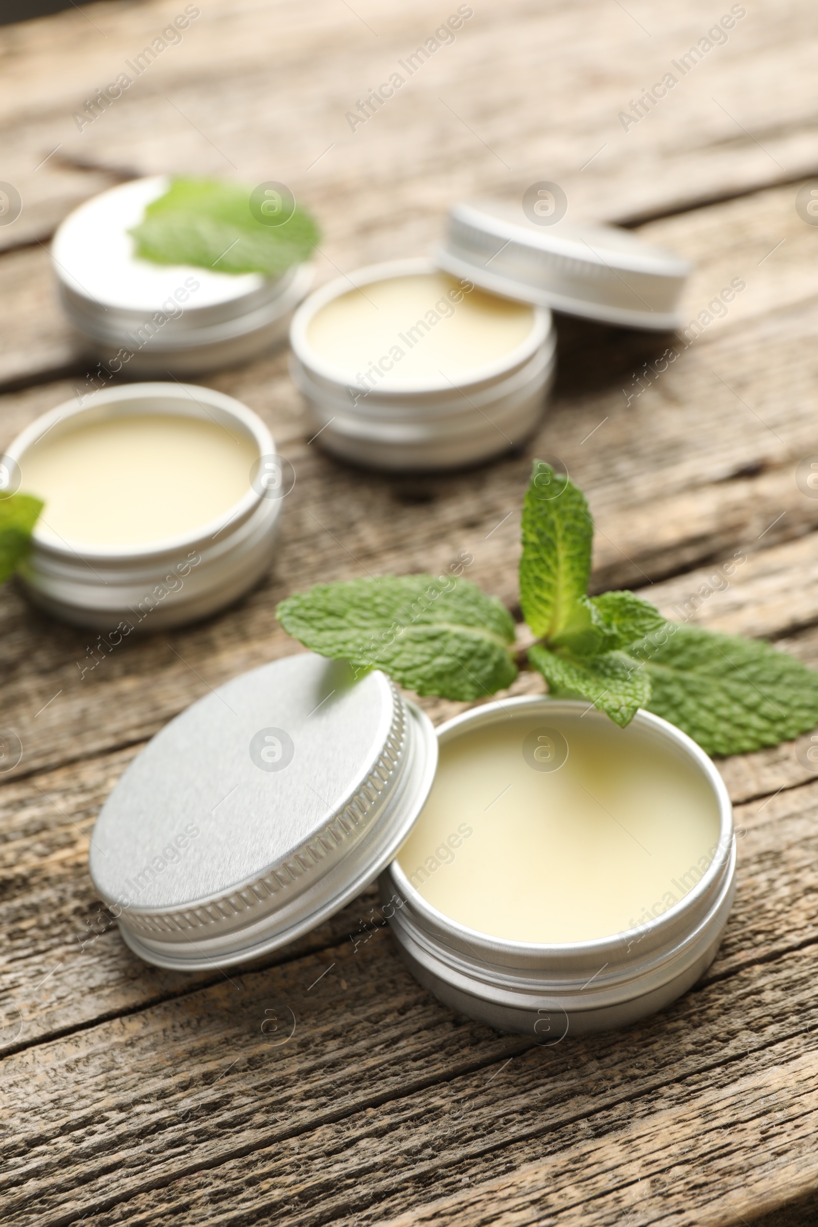 Photo of Natural lip balms and mint leaves on wooden background, selective focus