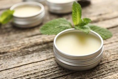 Photo of Natural lip balms and mint leaves on wooden background, selective focus. Space for text