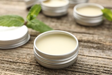 Photo of Natural lip balms and mint leaves on wooden background, selective focus