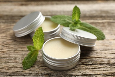 Photo of Natural lip balms and mint leaves on wooden background, selective focus