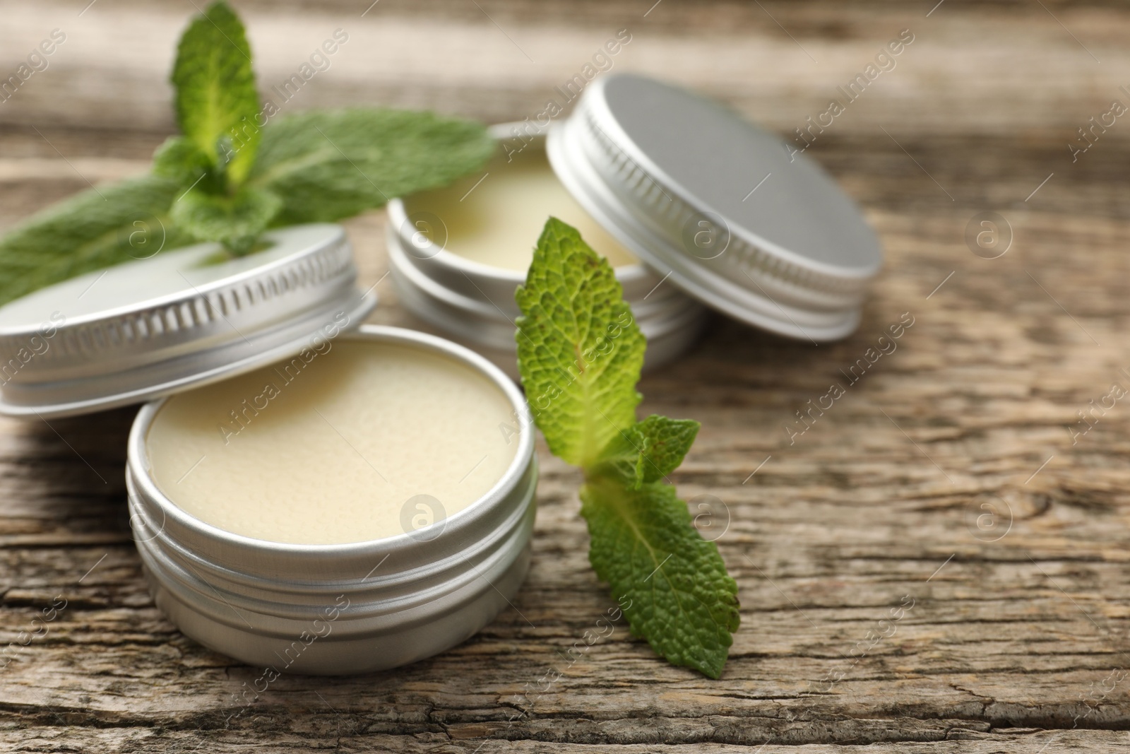 Photo of Natural lip balms and mint leaves on wooden background, selective focus