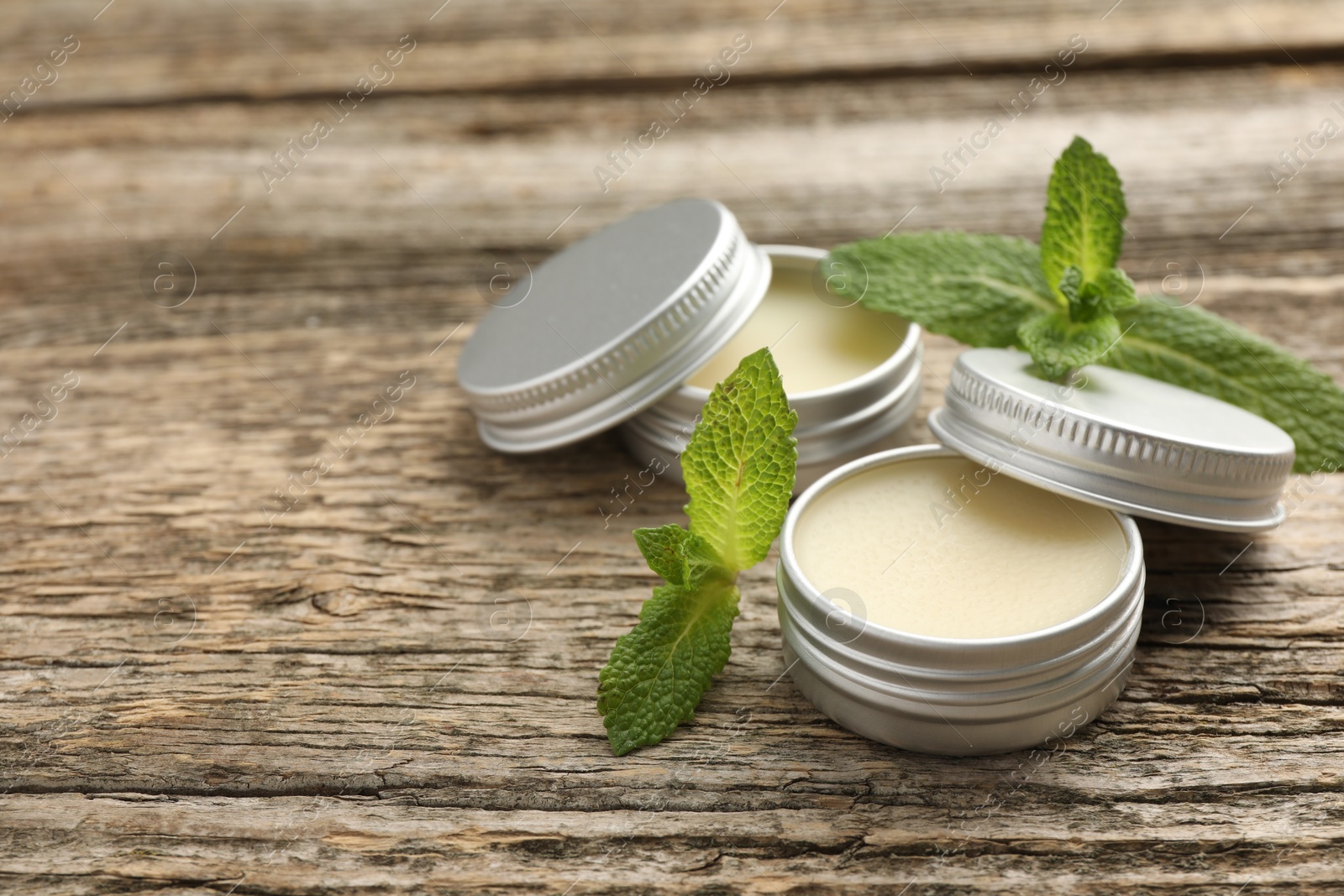 Photo of Natural lip balms and mint leaves on wooden background. Space for text