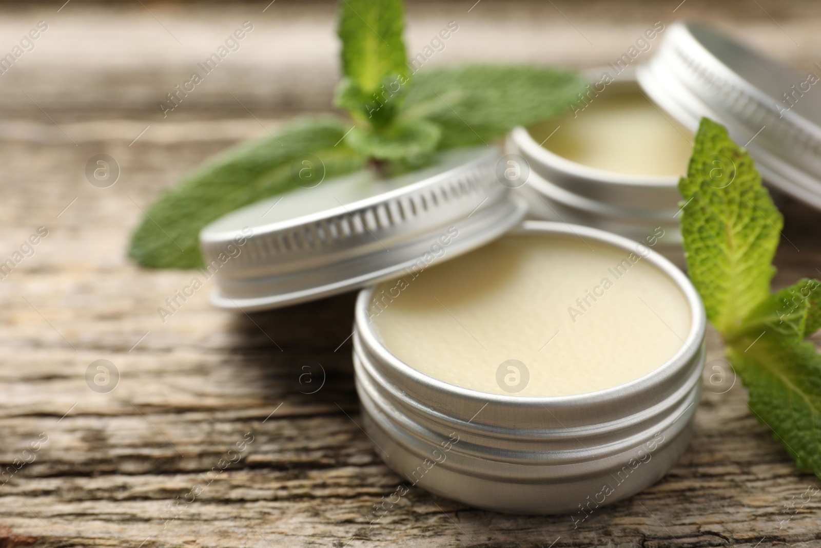 Photo of Natural lip balms and mint leaves on wooden background, selective focus