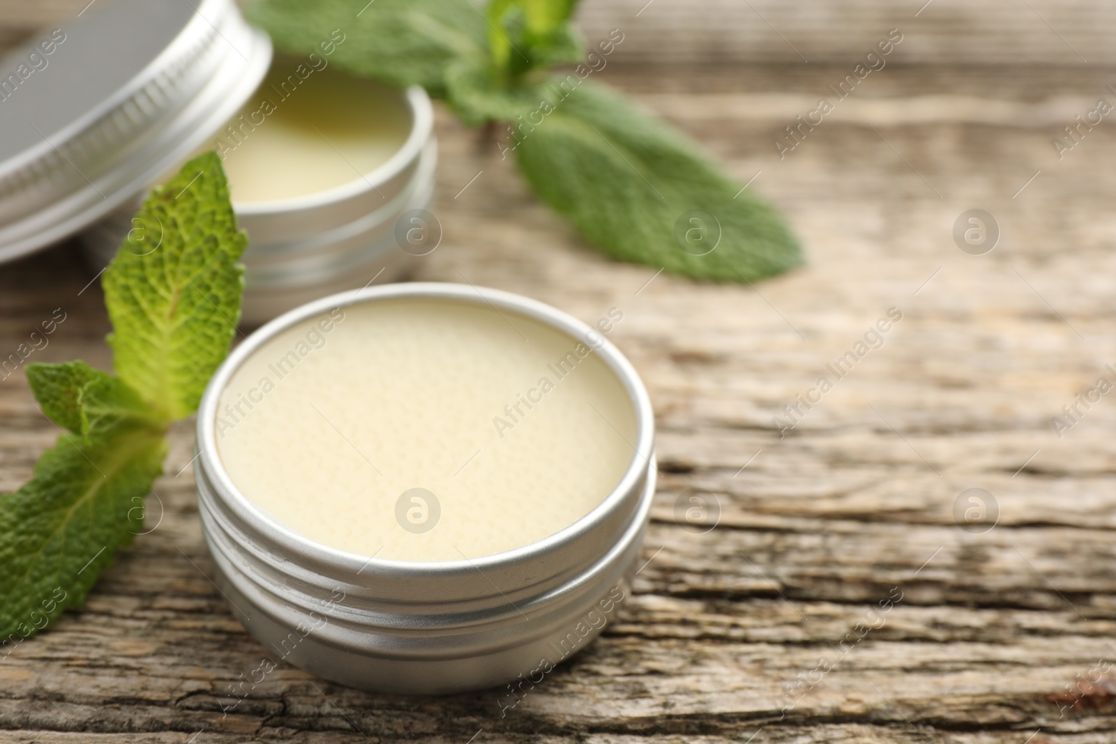 Photo of Natural lip balms and mint leaves on wooden background, selective focus. Space for text