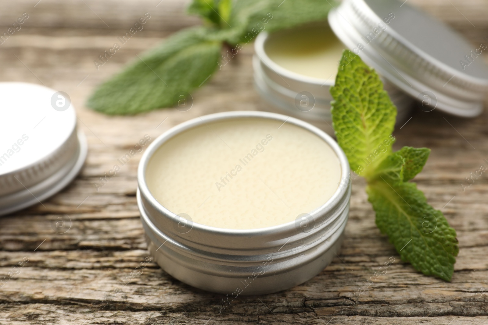 Photo of Natural lip balms and mint leaves on wooden background, selective focus