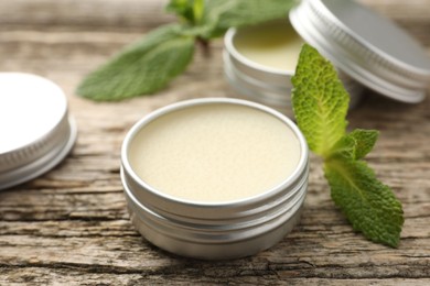 Photo of Natural lip balms and mint leaves on wooden background, selective focus