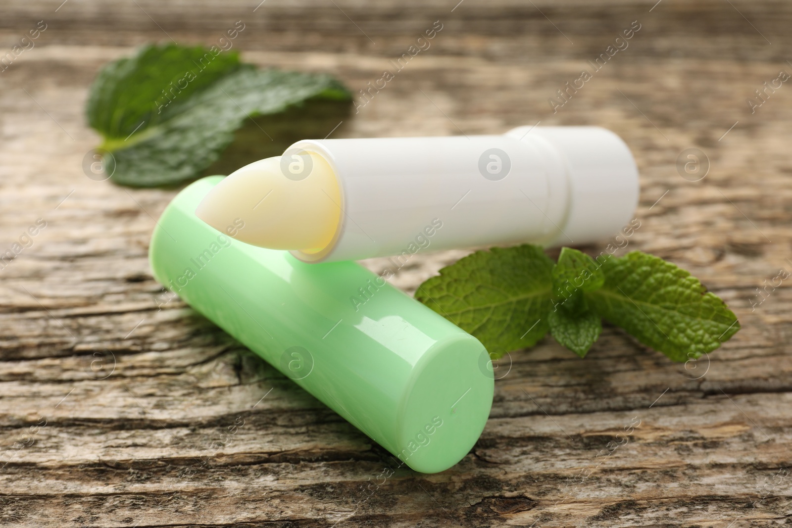 Photo of Natural lip balm and mint leaves on wooden background, closeup