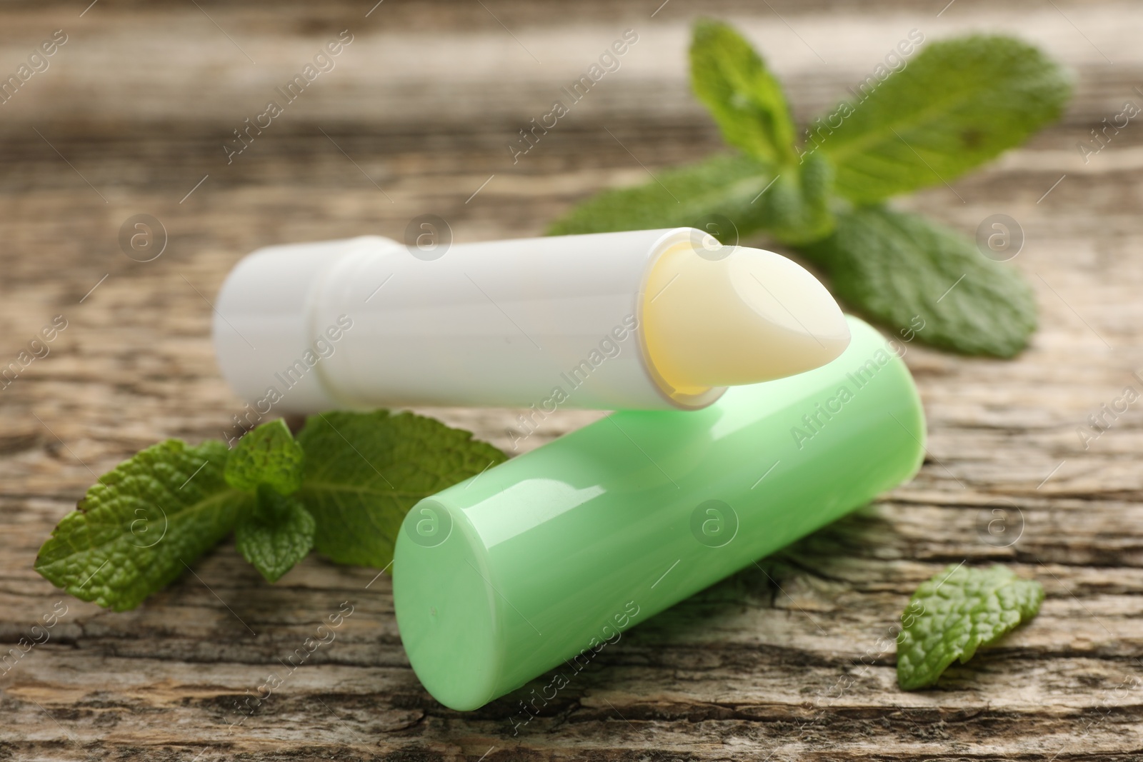 Photo of Natural lip balm and mint leaves on wooden background, closeup