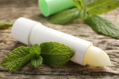 Photo of Natural lip balm and mint leaves on wooden background, closeup