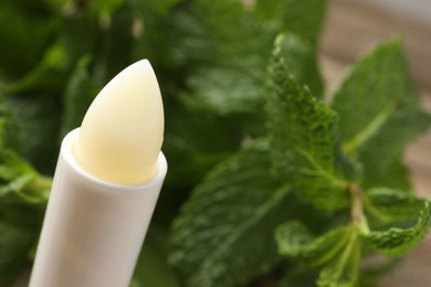 Photo of Natural lip balm and mint leaves on blurred background, closeup. Space for text