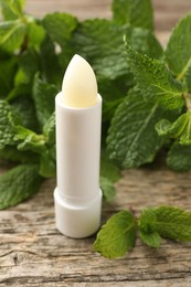 Photo of Natural lip balm and mint leaves on wooden background, closeup