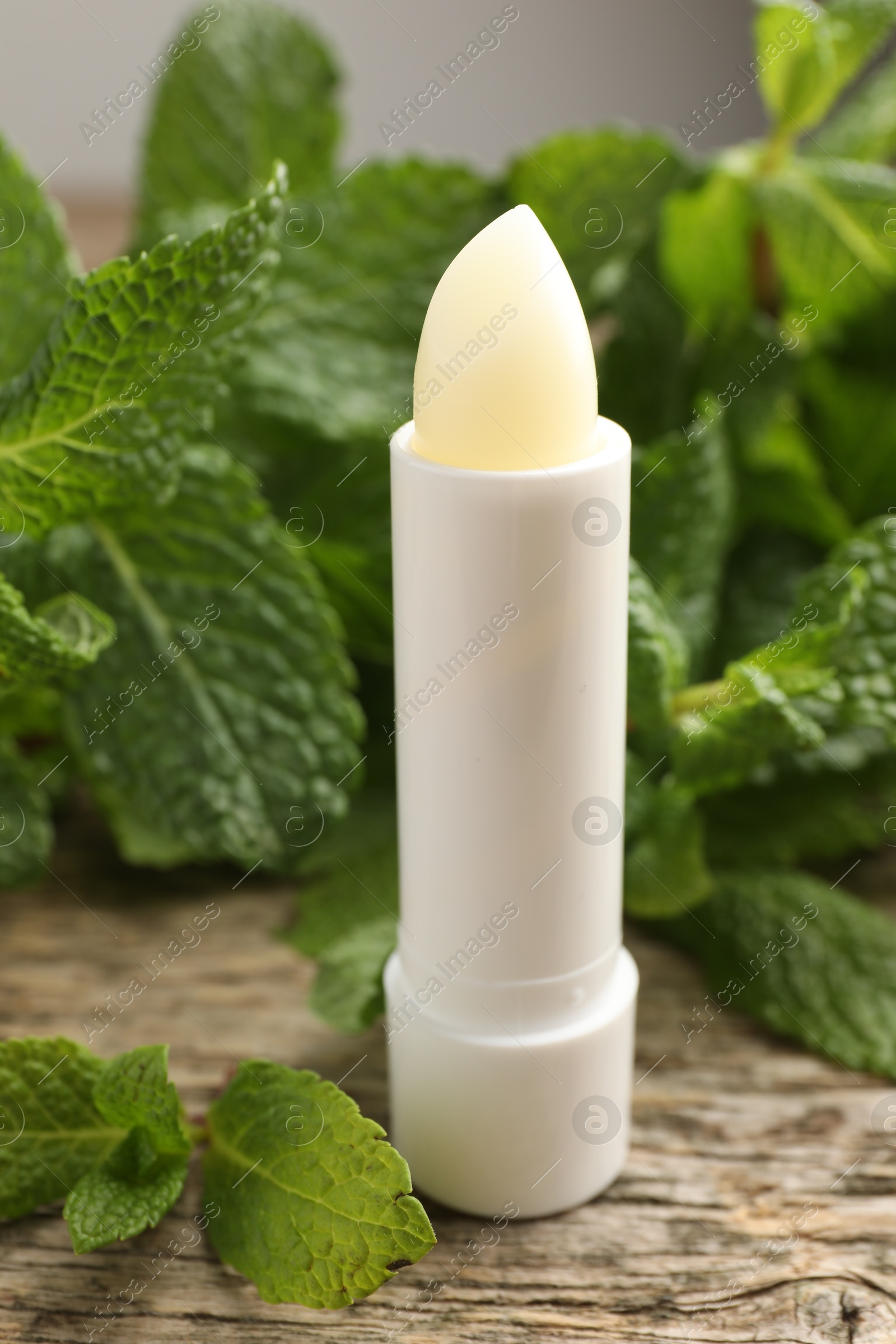 Photo of Natural lip balm and mint leaves on wooden background, closeup