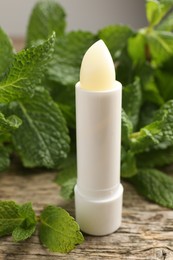 Photo of Natural lip balm and mint leaves on wooden background, closeup