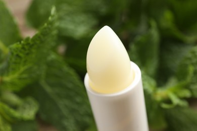 Photo of Natural lip balm and mint leaves on blurred background, closeup