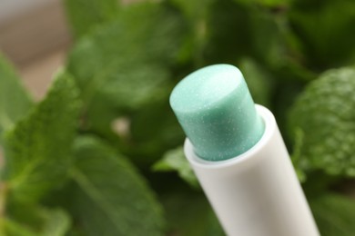 Photo of Natural lip balm and mint leaves on blurred background, closeup. Space for text