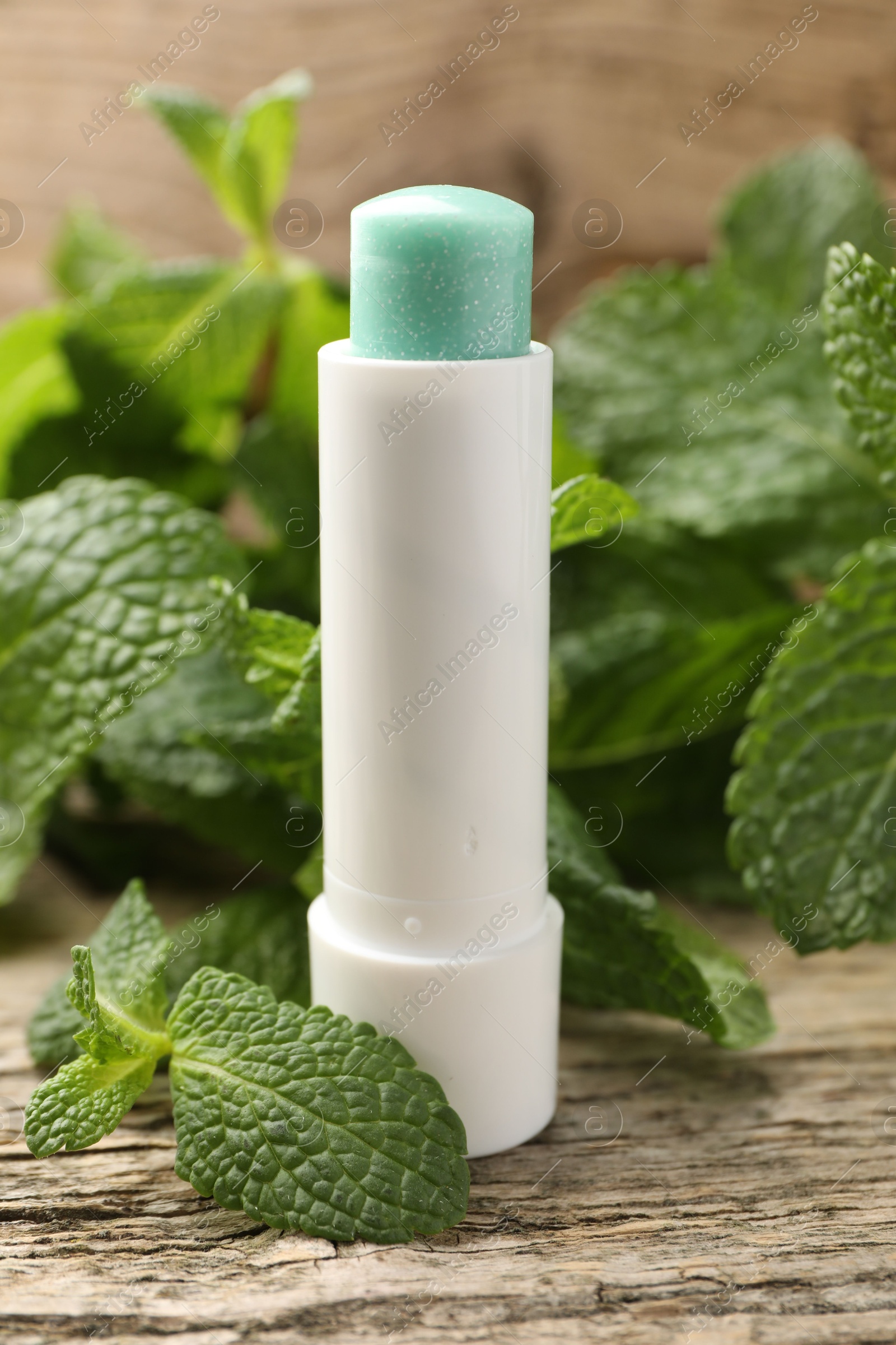 Photo of Natural lip balm and mint leaves on wooden background, closeup