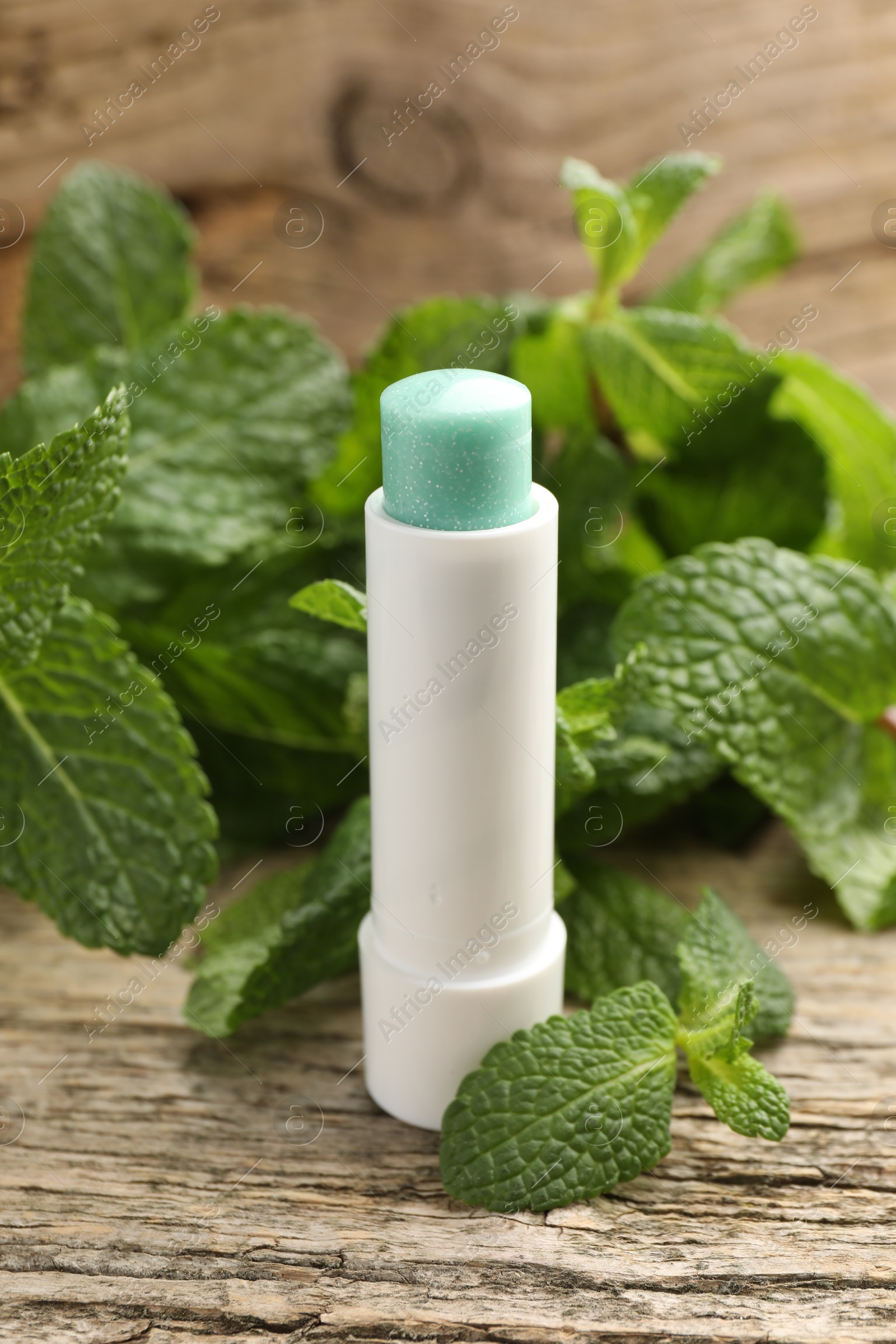 Photo of Natural lip balm and mint leaves on wooden background, closeup