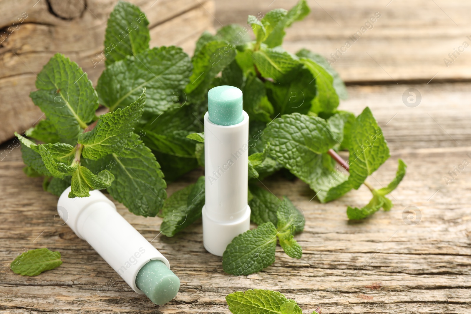 Photo of Natural lip balms and mint leaves on wooden background