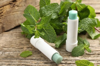 Photo of Natural lip balms and mint leaves on wooden background