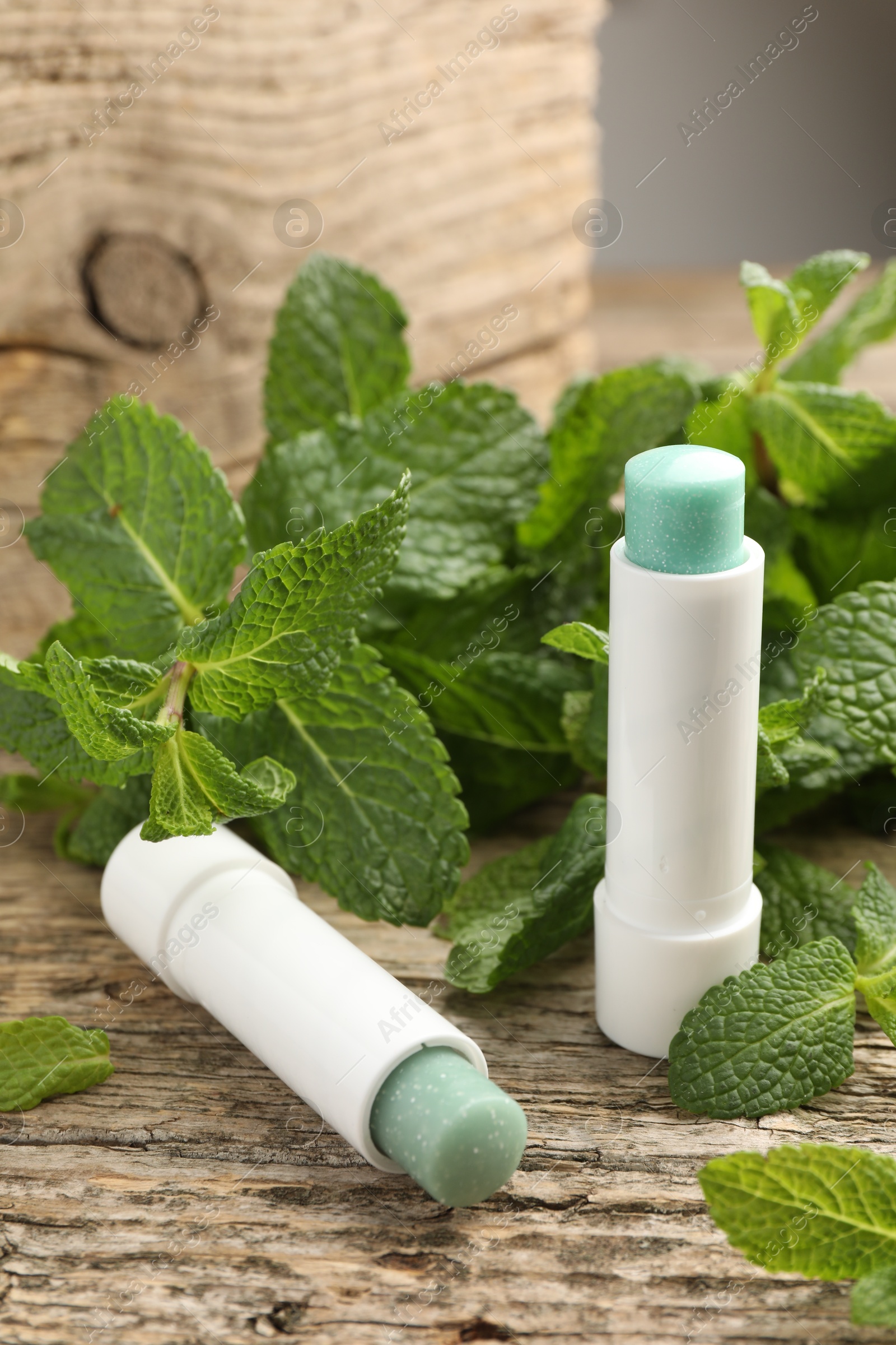 Photo of Natural lip balms and mint leaves on wooden background