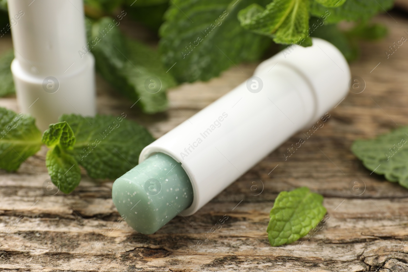 Photo of Natural lip balm and mint leaves on wooden background, closeup