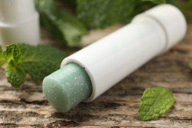 Photo of Natural lip balm and mint leaves on wooden background, closeup