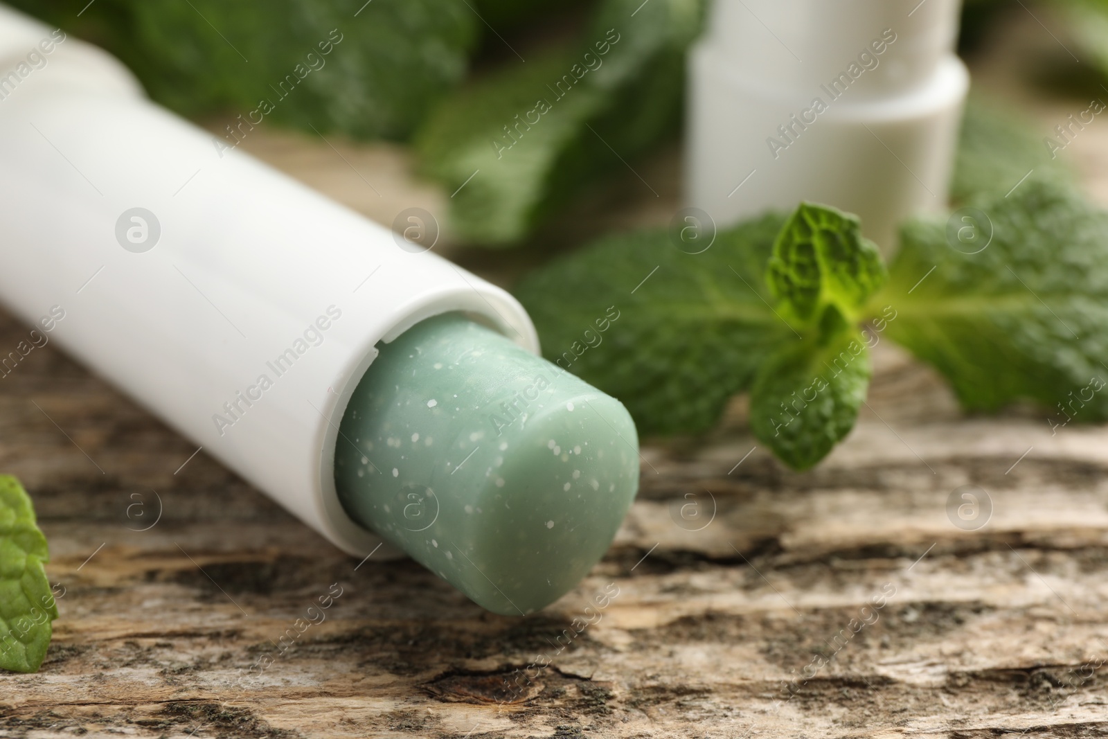 Photo of Natural lip balm and mint leaves on wooden background, closeup