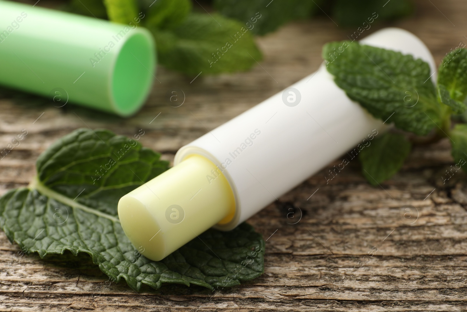 Photo of Natural lip balm and mint leaves on wooden background, closeup