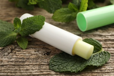 Photo of Natural lip balm and mint leaves on wooden background, closeup