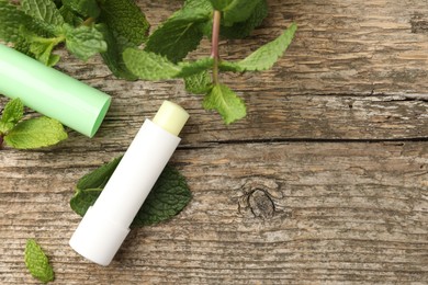 Photo of Natural lip balm and mint leaves on wooden background, flat lay. Space for text