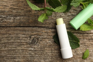 Photo of Natural lip balm and mint leaves on wooden background, flat lay. Space for text