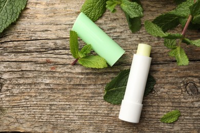 Photo of Natural lip balm and mint leaves on wooden background, flat lay. Space for text