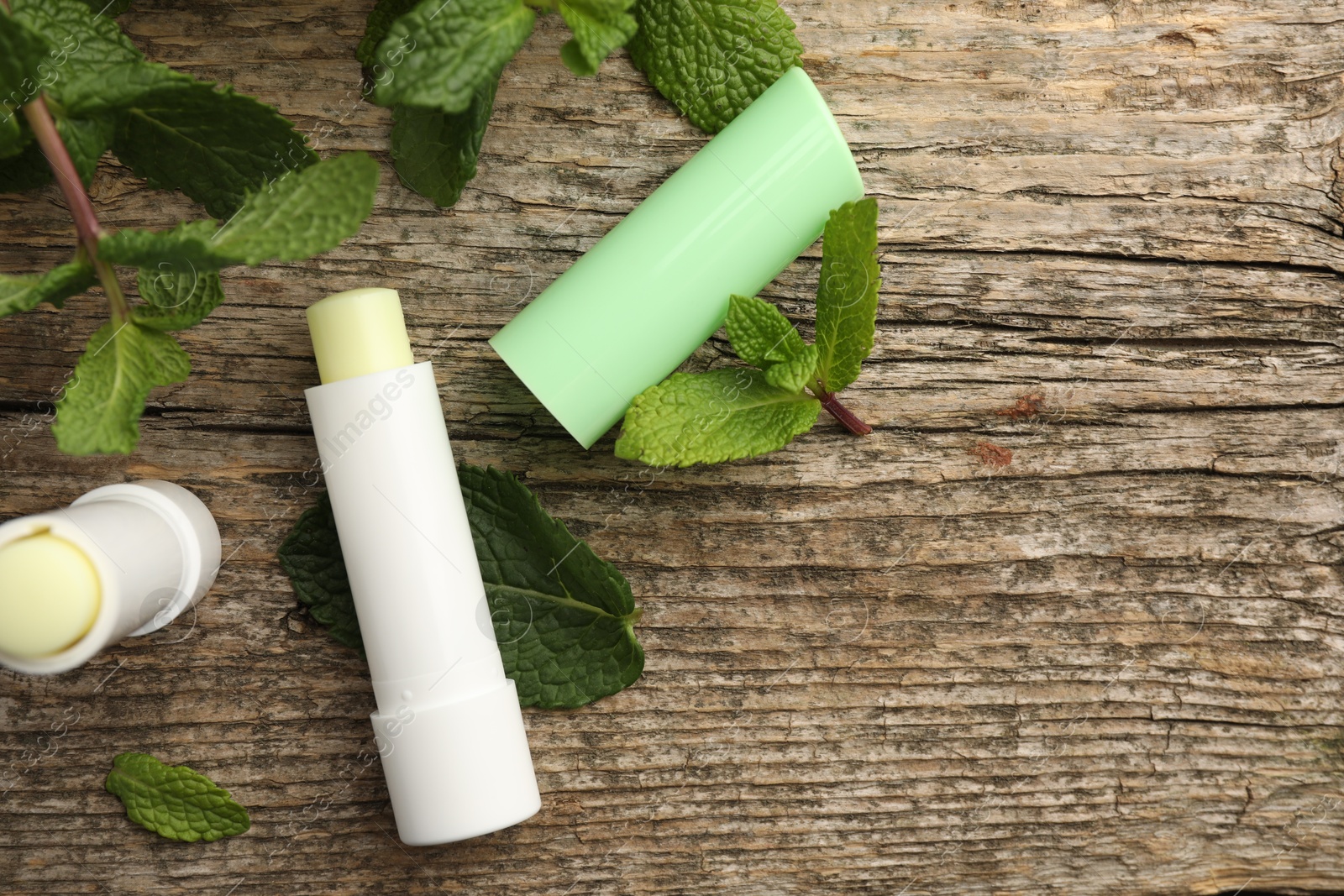 Photo of Natural lip balms and mint leaves on wooden background, flat lay. Space for text