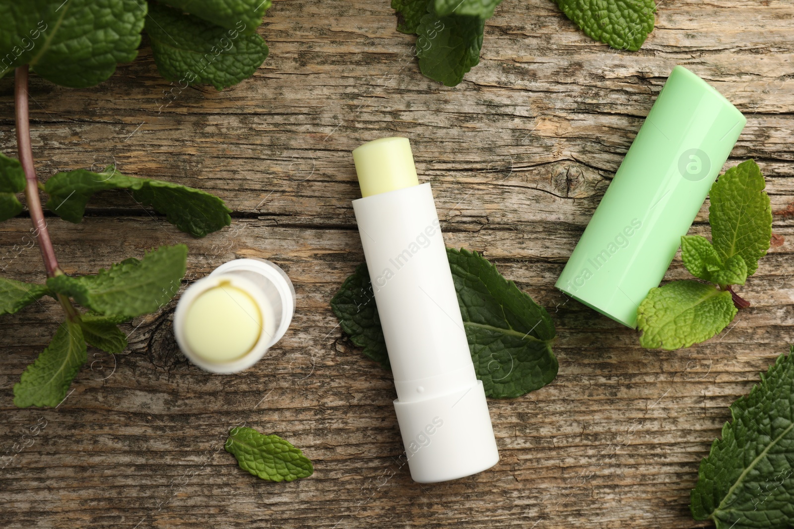 Photo of Natural lip balms and mint leaves on wooden background, flat lay