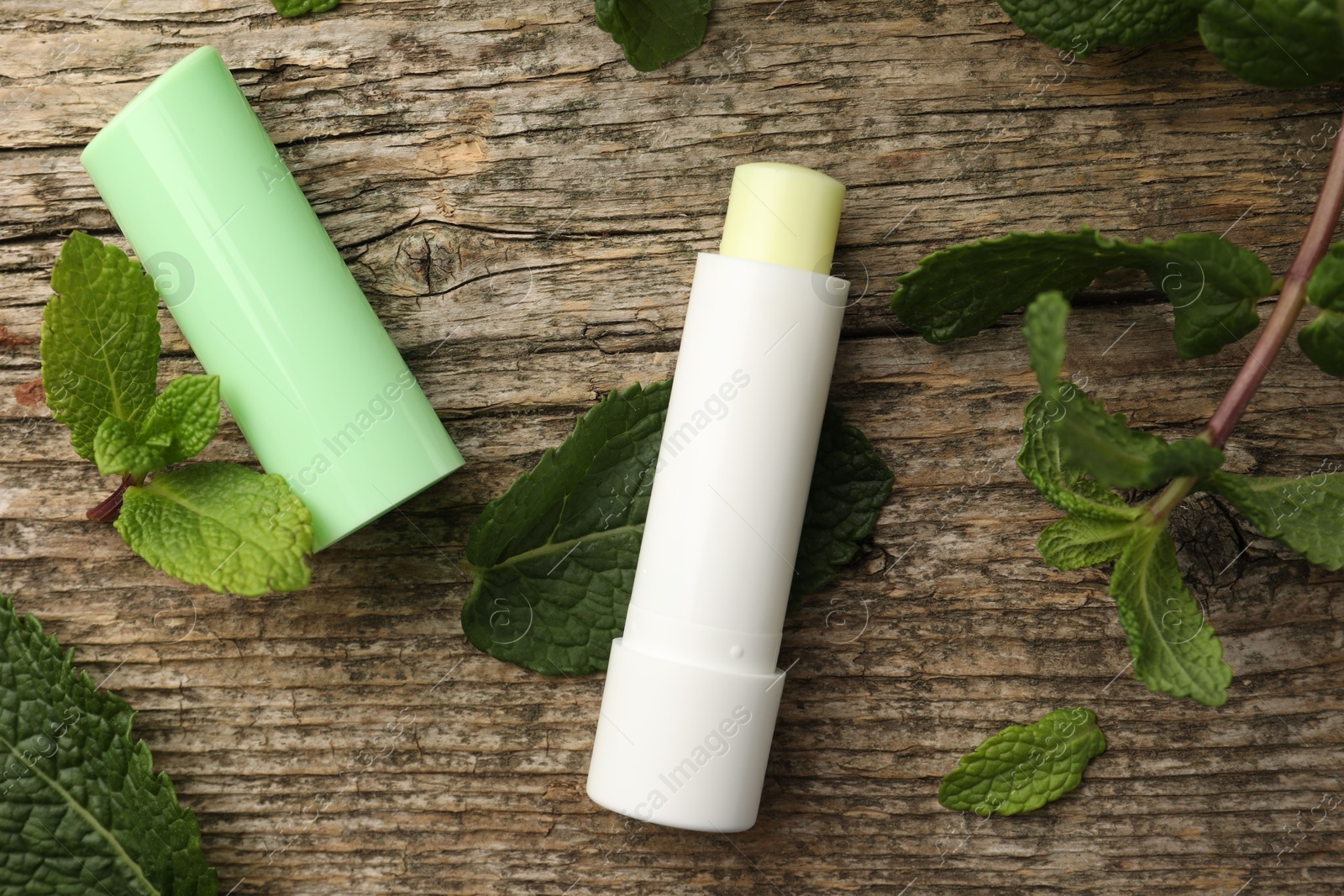 Photo of Natural lip balm and mint leaves on wooden background, flat lay