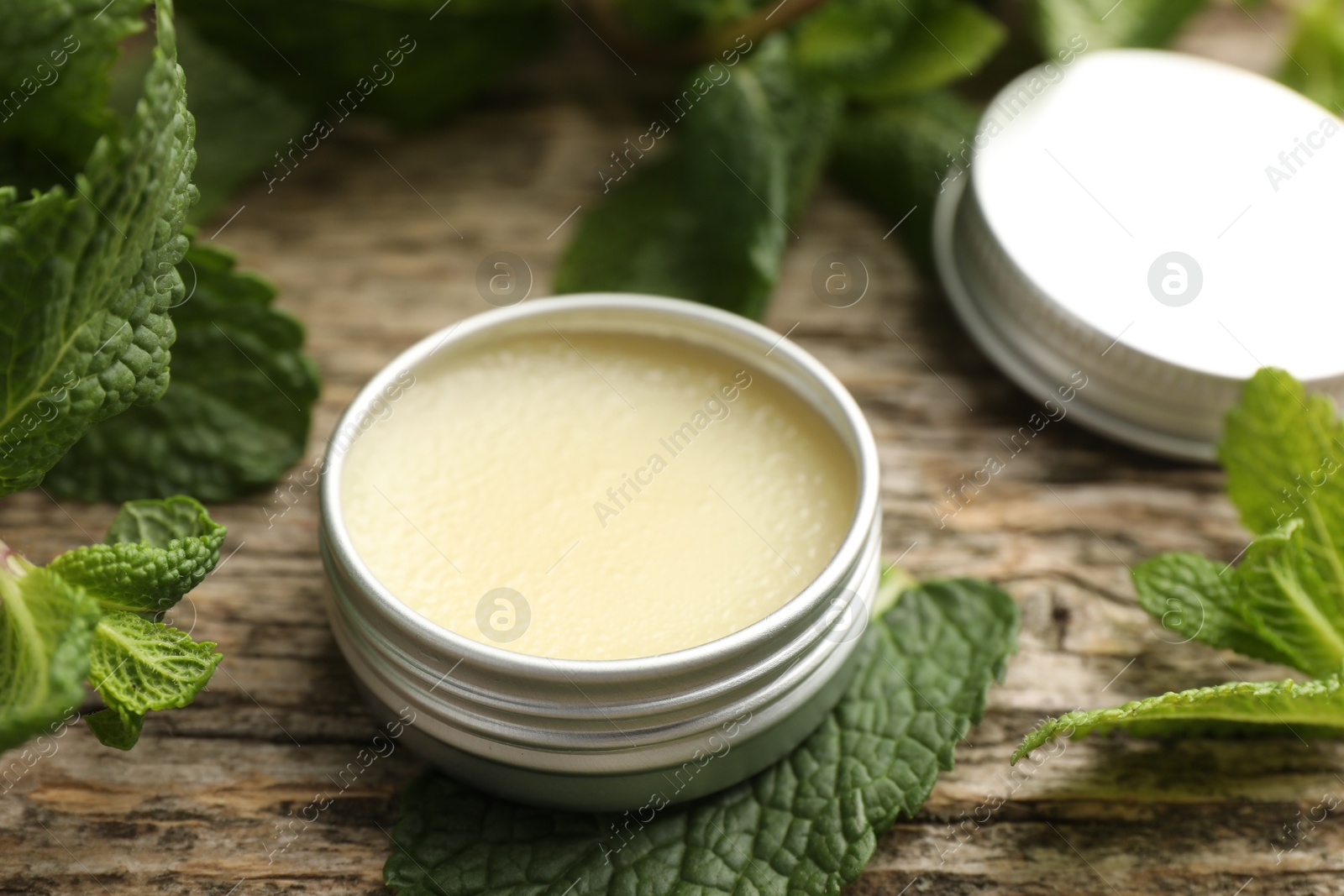 Photo of Natural lip balm and mint leaves on wooden background, closeup