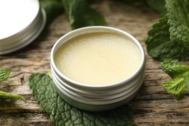 Photo of Natural lip balm and mint leaves on wooden background, closeup