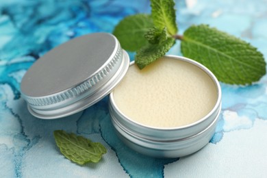 Photo of Natural lip balm and mint leaves on color background, closeup